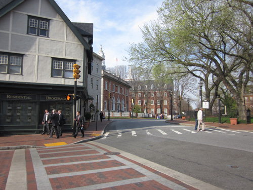 Church Circle: Three photos show a brick crosswalk at a signalized intersection.  The sidewalks are all made of red brick, and at the curb the bricks are laid to form a slope about 4 feet wide down to the street.  Where it meets the street is a detectable warning (DW) about 2 feet deep and 4 feet wide.  The bright yellow surface of the DW has peeled back or eroded at the top of one of the ramps revealing a few inches of white cement.